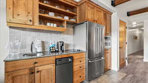 Kitchen with tasteful backsplash, beam ceiling, light hardwood flooring, sink, and dark stone counters