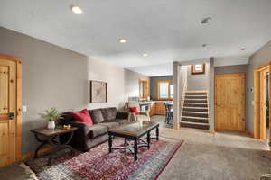 Living area with stairs, light colored carpet, a textured ceiling, recessed lighting, and baseboards