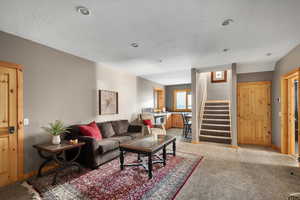 Living area with stairway, light carpet, a textured ceiling, and baseboards