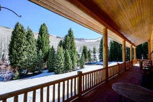 Snow covered deck featuring a mountain view, covered porch, and a forest view