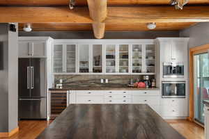 Kitchen with stainless steel appliances, beverage cooler, dark countertops, light wood-type flooring, and glass insert cabinets