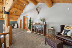 Living area featuring wood ceiling, carpet flooring, beamed ceiling, baseboards, and high vaulted ceiling