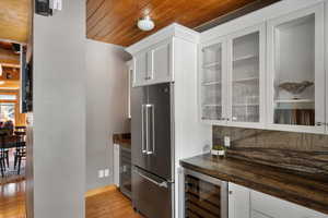 Kitchen with high quality fridge, wine cooler, light wood-style flooring, wood ceiling, and glass insert cabinets