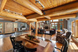 Dining space featuring wood ceiling, wood-type flooring, a stone fireplace, track lighting, and beam ceiling