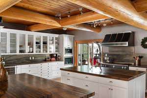 Kitchen featuring butcher block counters, wall chimney range hood, beverage cooler, decorative backsplash, and wooden ceiling