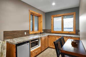 Kitchen featuring refrigerator, stainless steel microwave, backsplash, a sink, and healthy amount of natural light