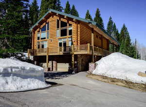 View of property exterior with log exterior, stone siding, a garage, and driveway