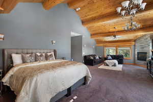 Carpeted bedroom with a chandelier, high vaulted ceiling, wood ceiling, a stone fireplace, and beamed ceiling