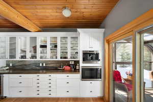 Bar area featuring black microwave, wood ceiling, tasteful backsplash, beam ceiling, and wood finished floors
