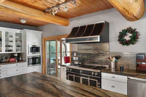 Kitchen featuring wall chimney exhaust hood, dark countertops, wooden ceiling, tasteful backsplash, and stainless steel appliances
