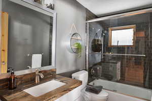 Full bathroom featuring toilet, shower / bath combination with glass door, and vanity