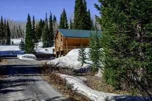 View of snow covered exterior featuring log exterior, metal roof, and a view of trees
