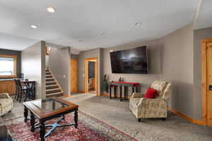 Carpeted living room featuring baseboards, recessed lighting, and stairway