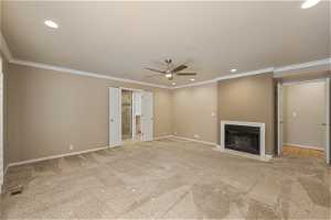 Large Primary Suite with gas fireplace, light carpet, crown molding, and ceiling fan