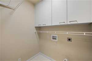 Main Floor Laundry featuring light tile flooring, cabinets, electric & gas dryer hookups, and washer hookup