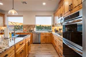 Kitchen with decorative light fixtures, light hardwood flooring, appliances with stainless steel finishes, backsplash, and sink