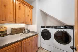 Laundry area featuring sink, light tile flooring, cabinets, and washing machine and clothes dryer