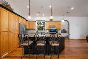 Kitchen featuring dark hardwood flooring, dark stone counters, a kitchen island, tasteful backsplash, and appliances with stainless steel finishes