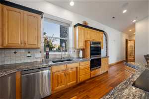 Kitchen featuring lofted ceiling, dark hardwood flooring, appliances with stainless steel finishes, backsplash, and sink