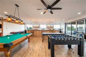 Recreation room with ceiling fan, billiards, bar, and light hardwood flooring