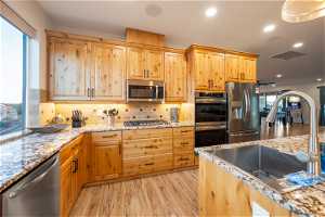 Kitchen featuring sink, backsplash, light hardwood flooring, light stone counters, and stainless steel appliances