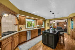 Kitchen with light hardwood / wood-style flooring, sink, a center island, decorative light fixtures, and black appliances