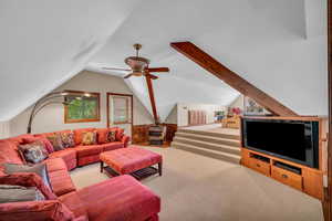 Carpeted living room featuring ceiling fan and vaulted ceiling