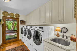 Laundry room with washer and dryer, a textured ceiling, light hardwood / wood-style floors, sink, and cabinets