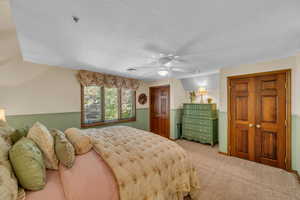 Bedroom with a textured ceiling, light colored carpet, and ceiling fan