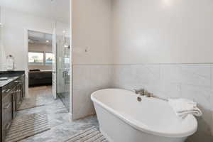 Bathroom with vanity, independent shower and bath, tile floors, ceiling fan, and tile walls