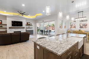 Kitchen featuring a tiled fireplace, light hardwood / wood-style flooring, an island with sink, decorative light fixtures, and ceiling fan