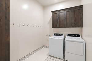 Clothes washing area with separate washer and dryer, cabinets, and light tile floors