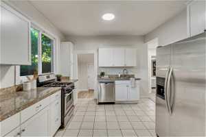 Kitchen with sink, white cabinets, light tile floors, stone counters, and appliances with stainless steel finishes
