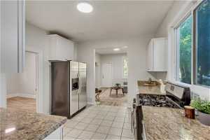 Kitchen featuring light tile floors, range with gas stovetop, white cabinetry, and stainless steel fridge