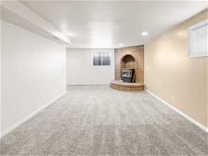 Unfurnished living room with light carpet, a textured ceiling, brick wall, and a fireplace
