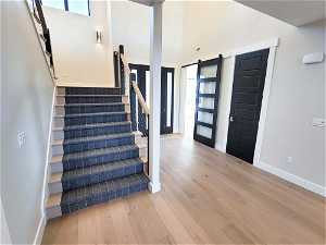 Stairs featuring a barn door, light hardwood / wood-style floors, and a towering ceiling