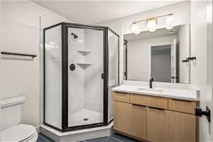 Bathroom featuring toilet, vanity, a shower with shower door, a textured ceiling, and tile floors