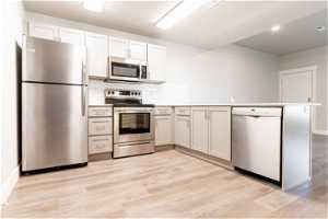 Kitchen with white cabinets, light hardwood flooring, tasteful backsplash, stainless steel appliances, and kitchen peninsula