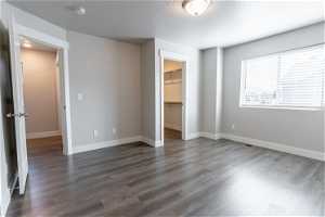 Unfurnished bedroom with a walk in closet, a textured ceiling, dark hardwood floors, and a closet