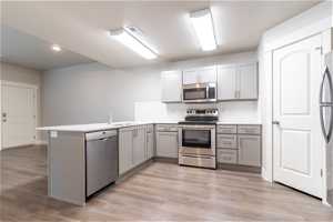 Kitchen featuring kitchen peninsula, tasteful backsplash, gray cabinetry, light hardwood flooring, and stainless steel appliances