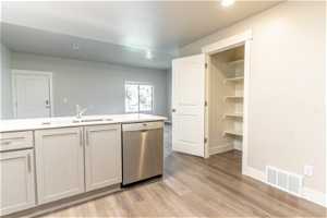 Kitchen featuring white cabinets, dishwasher, sink, and light hardwood flooring