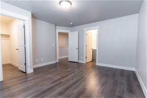 Unfurnished bedroom with ensuite bathroom, a walk in closet, a textured ceiling, dark hardwood floors, and a closet