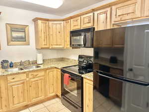 Kitchen with sink, light tile flooring, light stone countertops, and black appliances