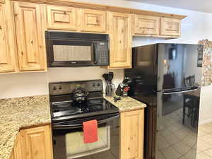 Kitchen featuring light stone counters, light tile floors, and black appliances