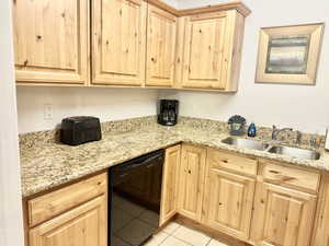 Kitchen with light tile floors, sink, light stone counters, and black dishwasher