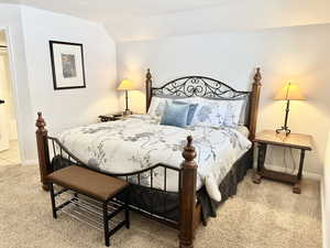 Carpeted bedroom featuring ensuite bathroom and vaulted ceiling