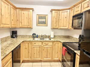 Kitchen with sink, light stone counters, light tile floors, and black appliances