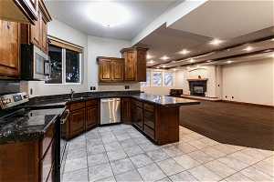 Kitchen with sink, a fireplace, dark stone countertops, appliances with stainless steel finishes, and kitchen peninsula