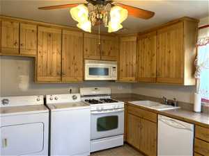Kitchen featuring light tile floors, white appliances, ceiling fan with notable chandelier, independent washer and dryer, and sink