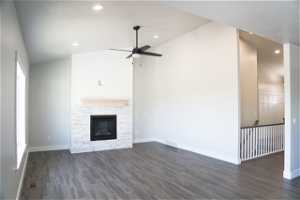 Unfurnished living room featuring vaulted ceiling, a fireplace, dark wood-type flooring, and ceiling fan